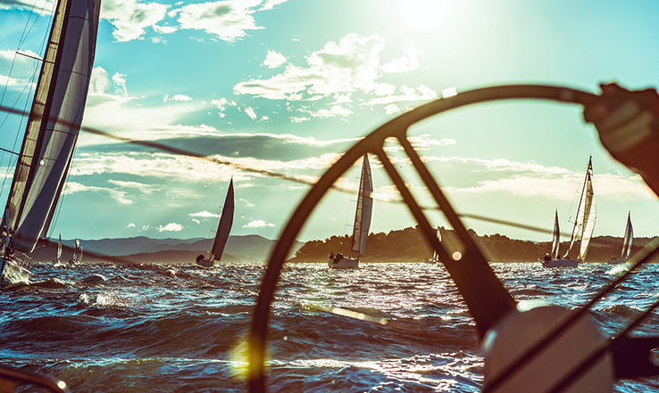 Sailor steering boat, racing other sail boats. 