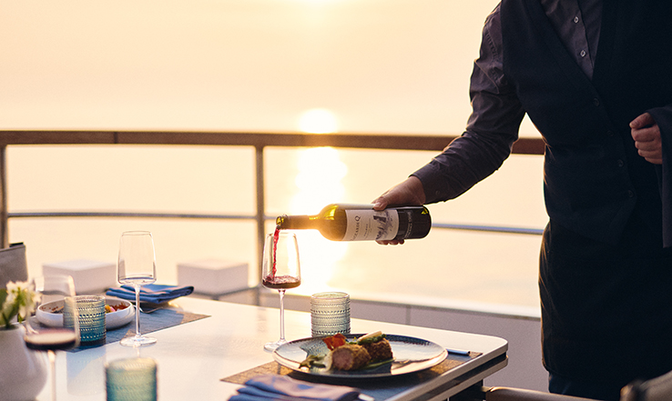 Person pouring wine into a glass at a table on a yacht. 
