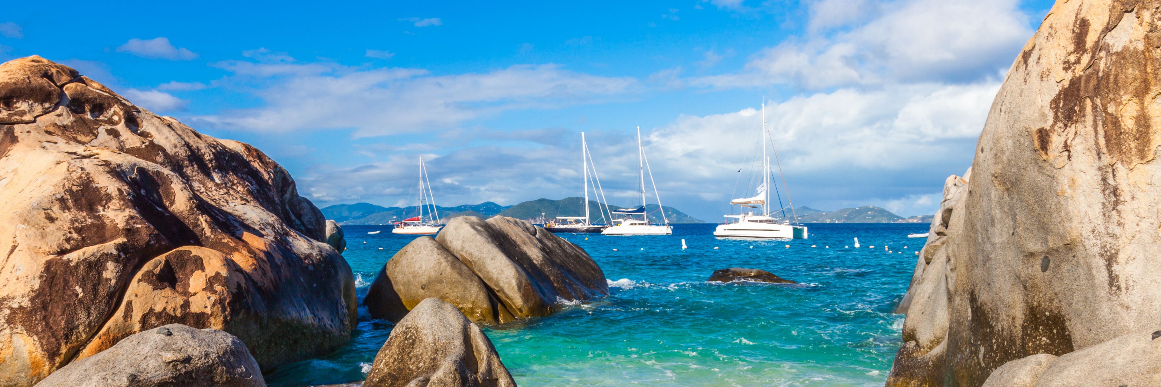 Large rocks in the ocean, overlooking some boats sailing in the distance. 