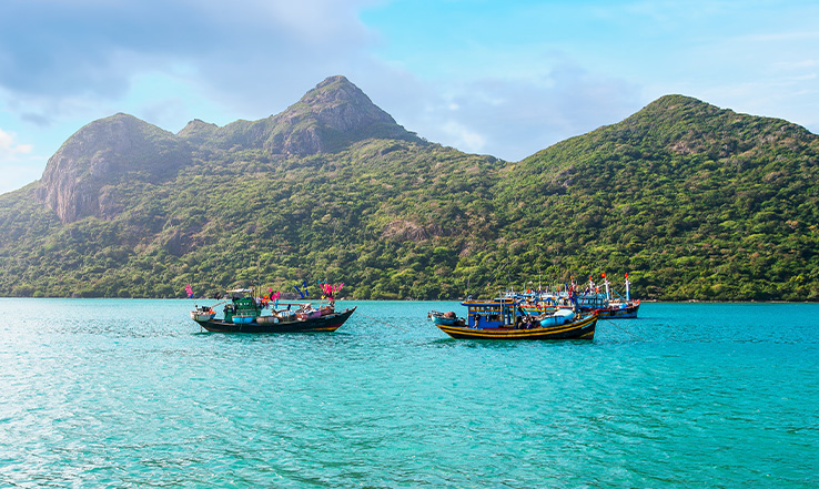 Three colorful boats sailing by an island. 