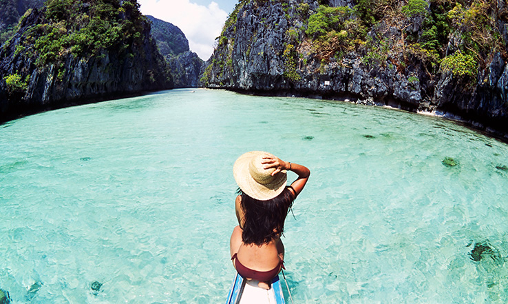 Woman on the front of a boat as they boat over clear water. 