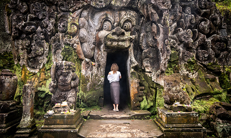 Woman at an open entrance to a rock structure with carvings on the outside. 