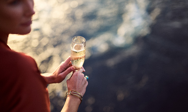 Person holding champagne over ocean water. 