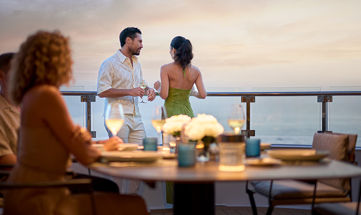 A couple conversing on a deck, overlooking the ocean. 