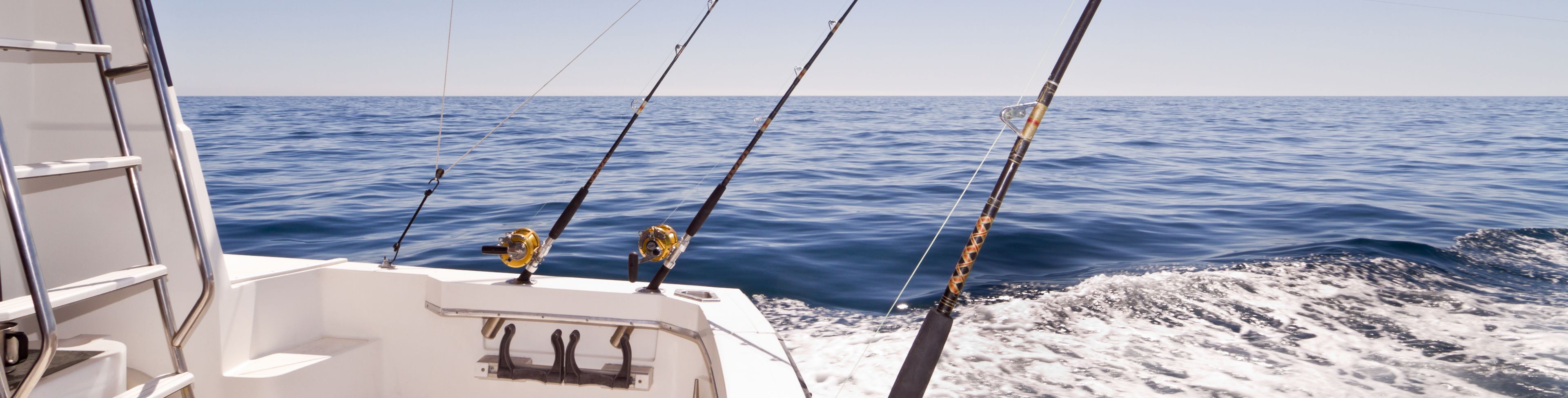 Back of boat with large fishing poles in the water that are attached to the boat. 