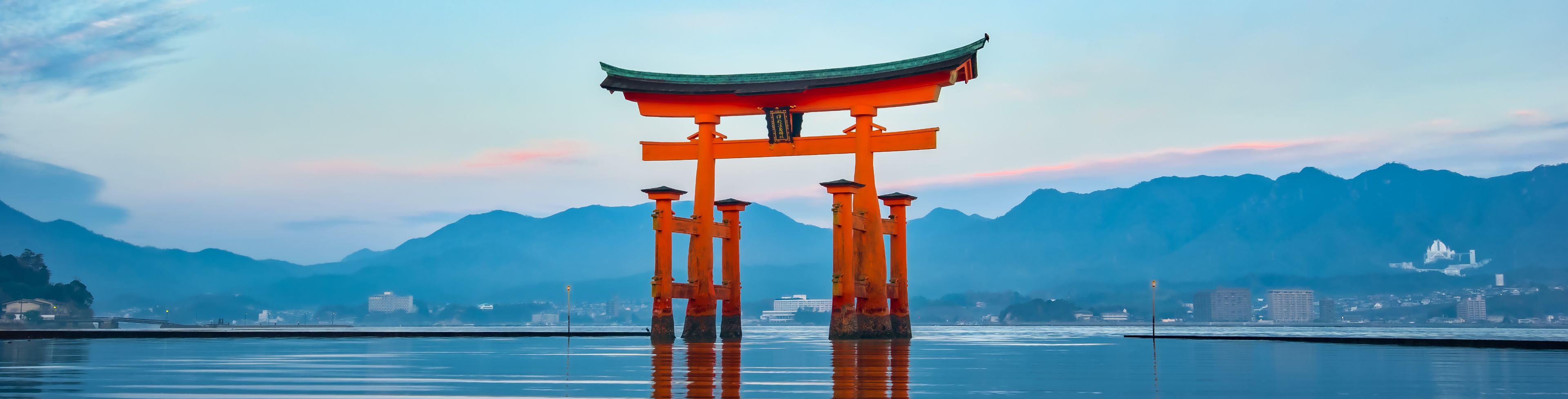 Shrine on the water with village and mountain in the background. 