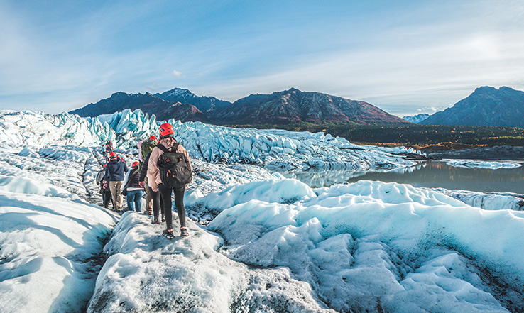 Multiple people walking in a line over snow and glaciers with guide. 