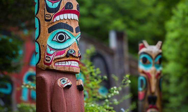 Totem poles with plants and wildlife surrounding them.