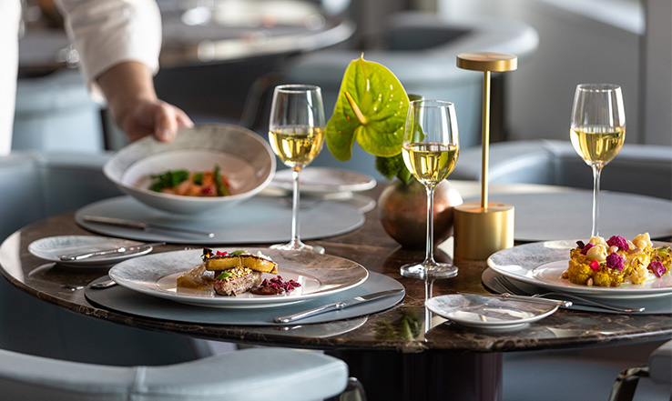 Person setting food on a table that has partially filled wine glasses.