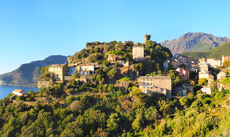 Corsica city surrounded by green treen overlooking the ocean near a cliffside. 