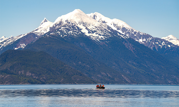 Small row boat on water with large mountain in the distance.