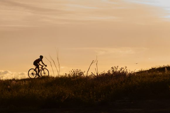 A person bikes with orange tinted skies in the background.