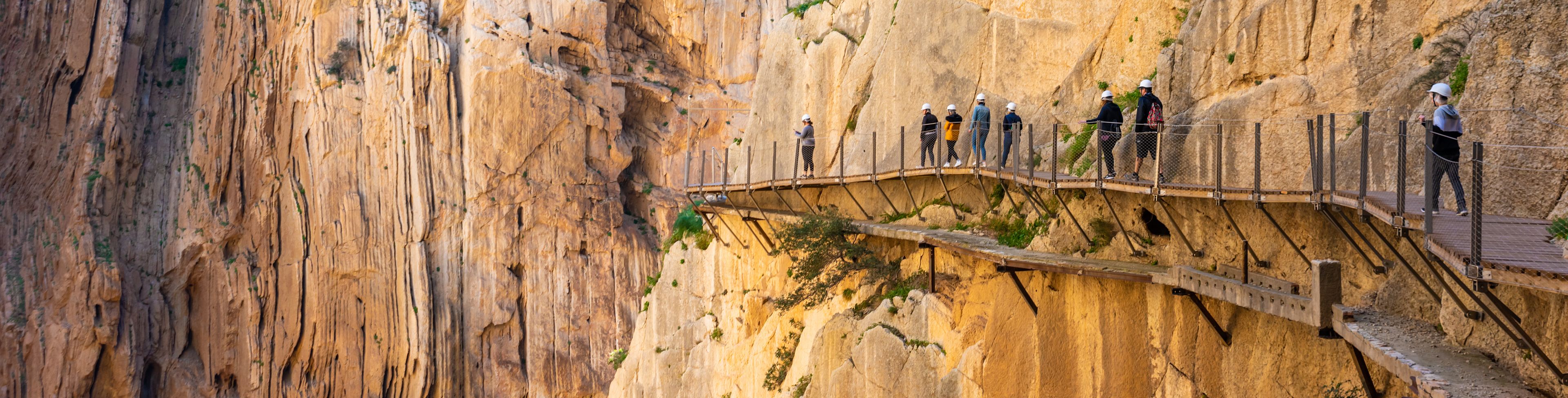 People cross a walkway attached to a rocky cliffside