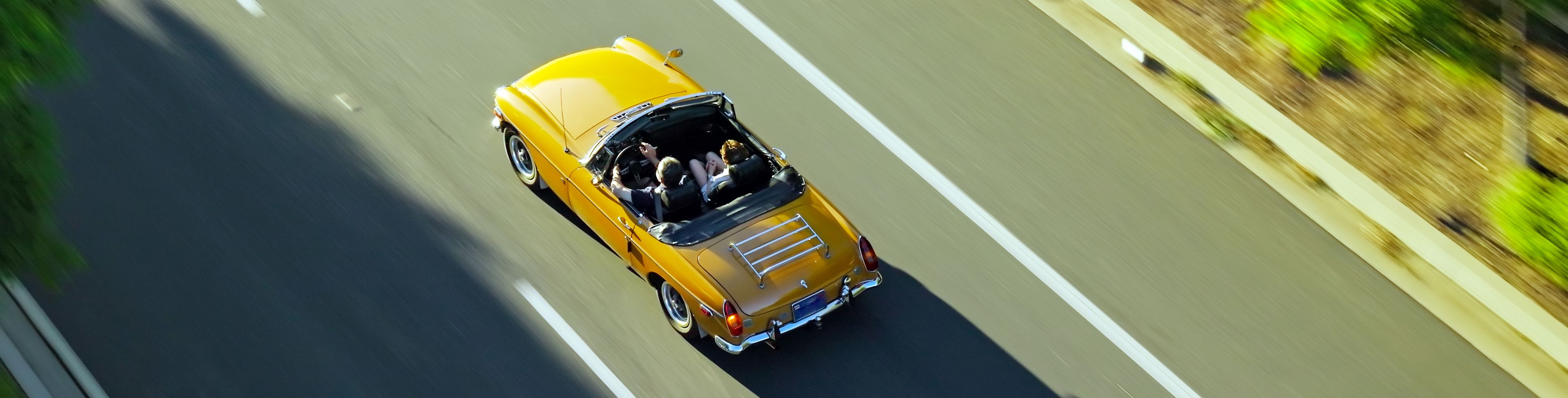 Sky view of a yellow convertible driving on a road. 