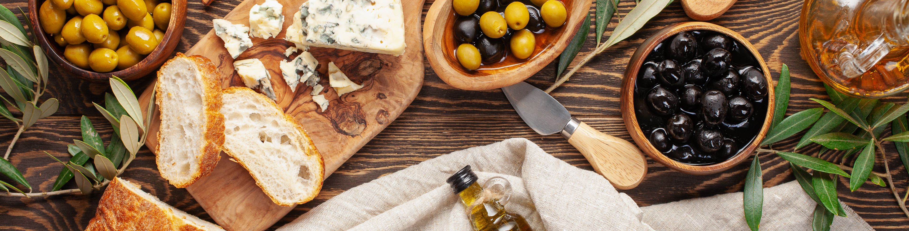 Bread, olives and olive oil sit on a wood table.