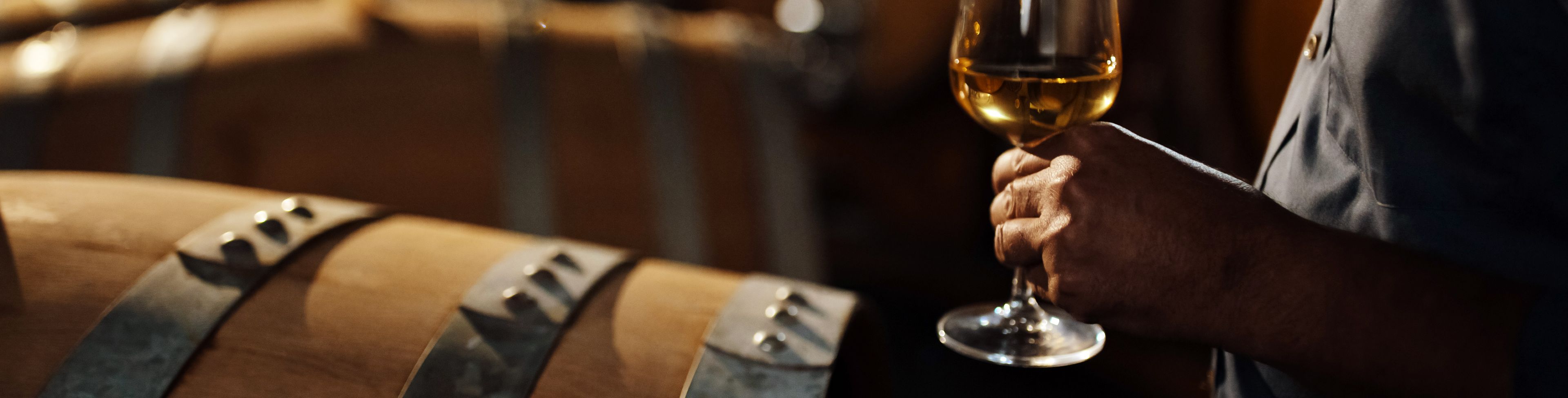 Person holding a glass of wine, near a barrel.