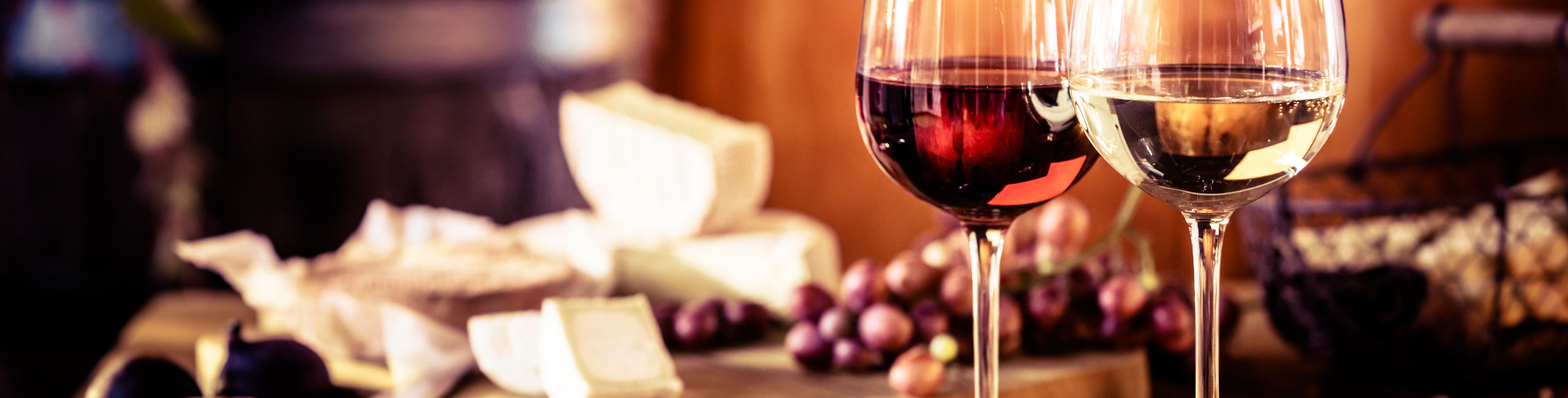 Two wind glasses set on a table with cheese and grapes.