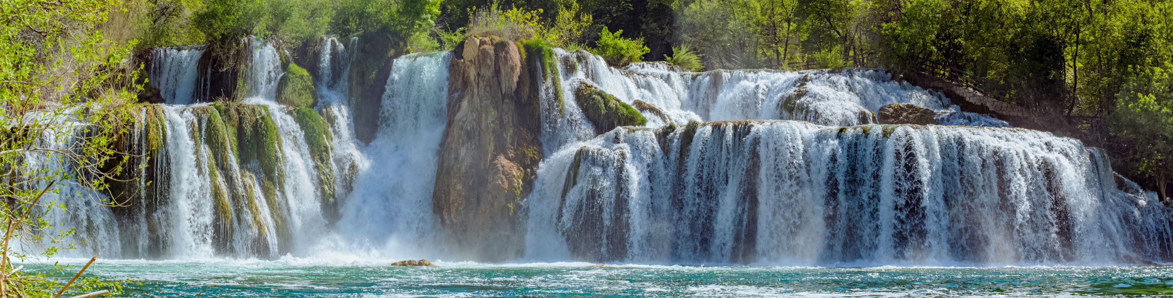 A large waterfall flows into teal waters below. 