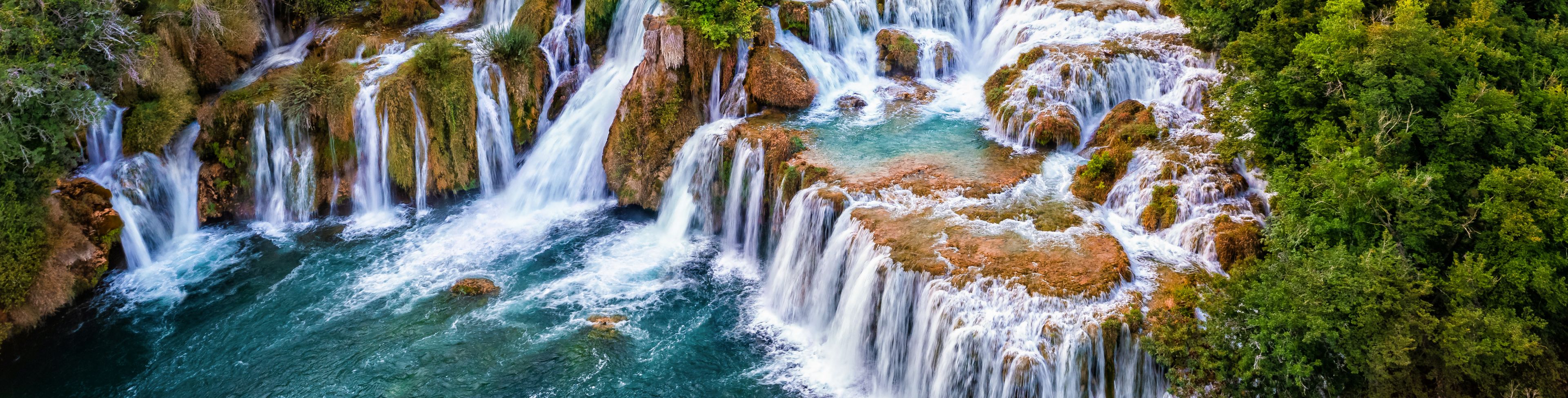 Aerial view of a cluster of waterfalls surrounded by a forest. 