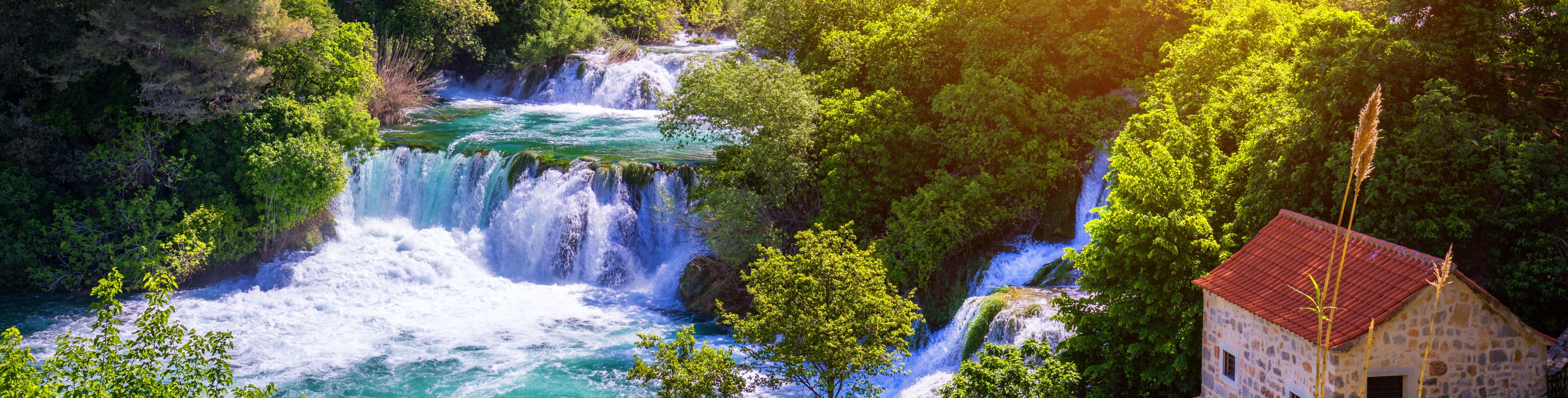 Waterfall in forest leading to a small cottage and land.