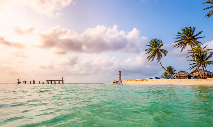 Woman walking into the clear blue ocean water from a white sandy beach.