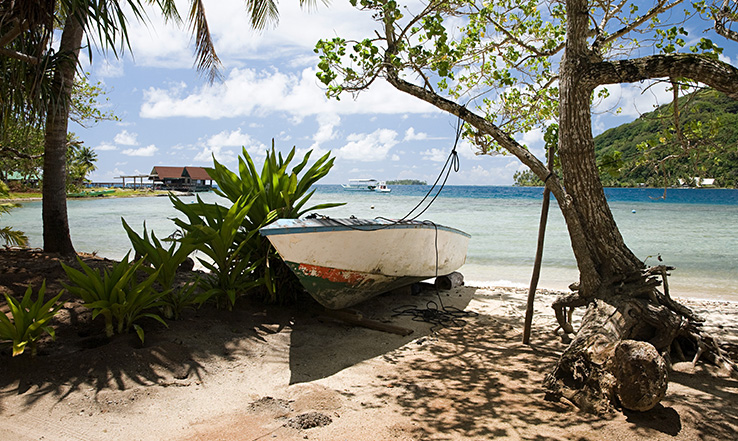 Small boat beached on the the island, with the beach and ocean in the distance. 