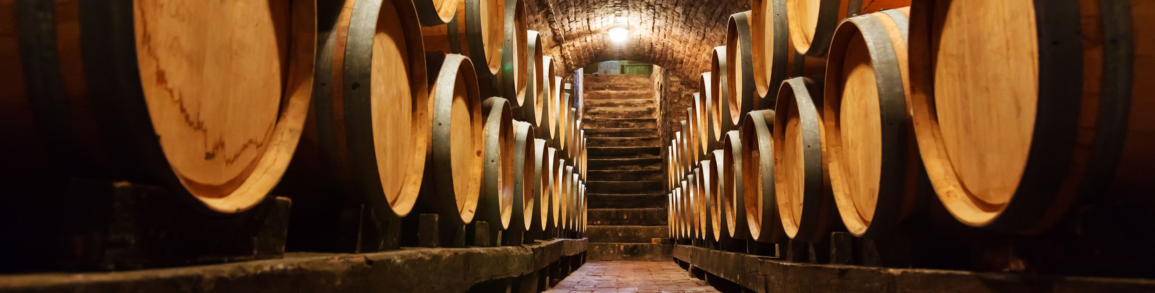 Walkway between many barrels of wine stacked on top of each other.