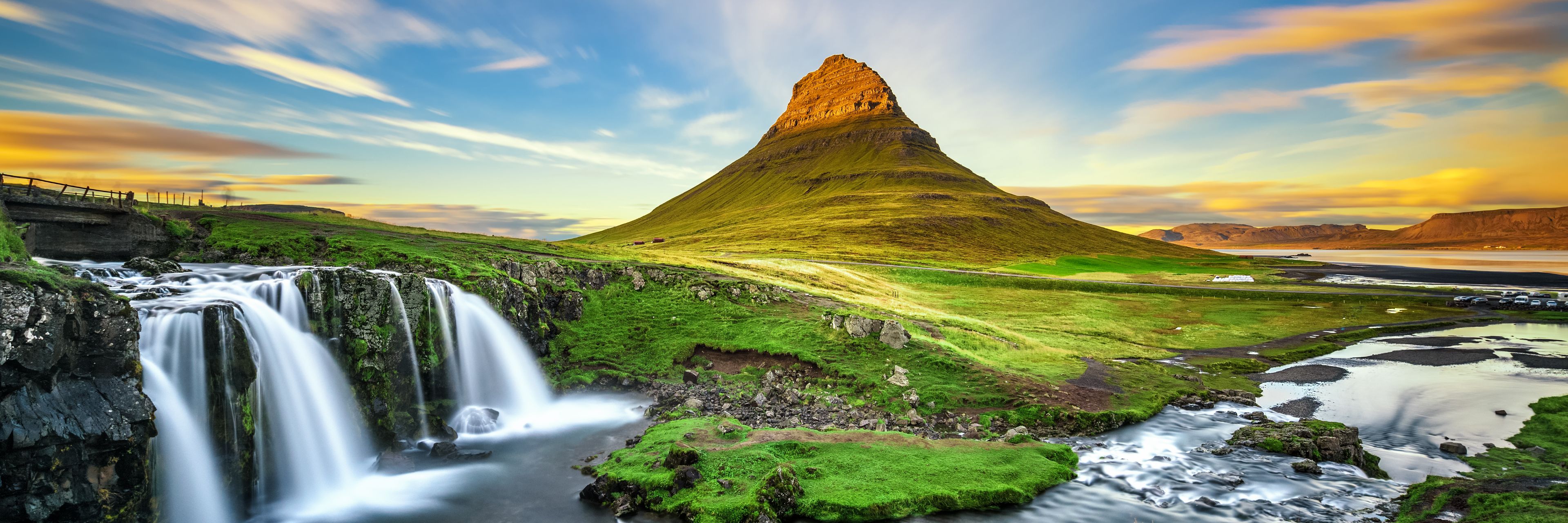 View of mountain and waterfalls, with nothing but green grass and nature surrounding them.