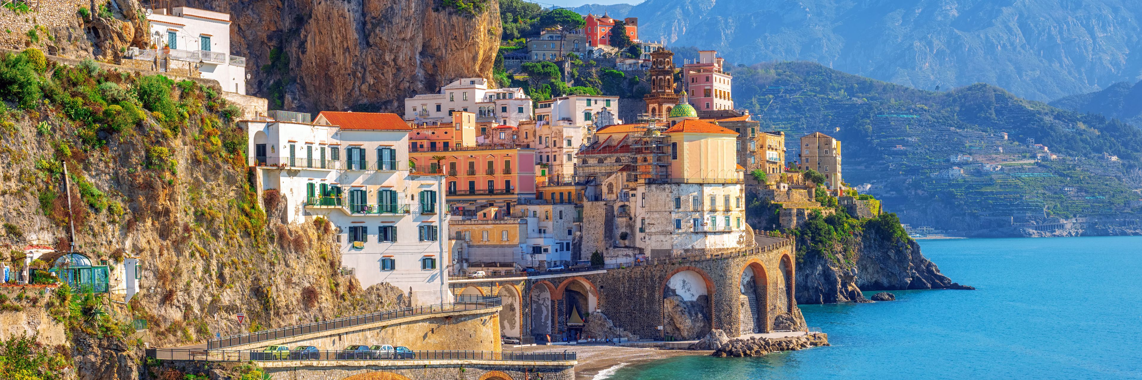 Buildings with winding road along cliffside above water.