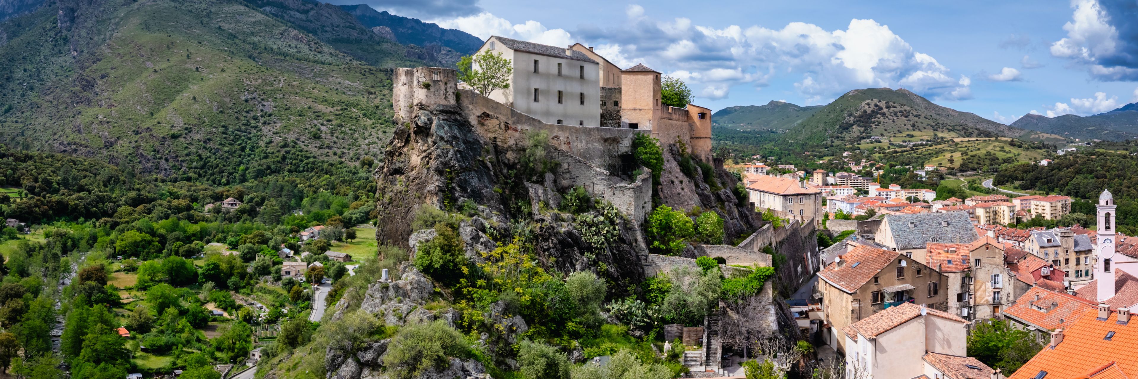 Old buildings on the top of a cliff and a town below.