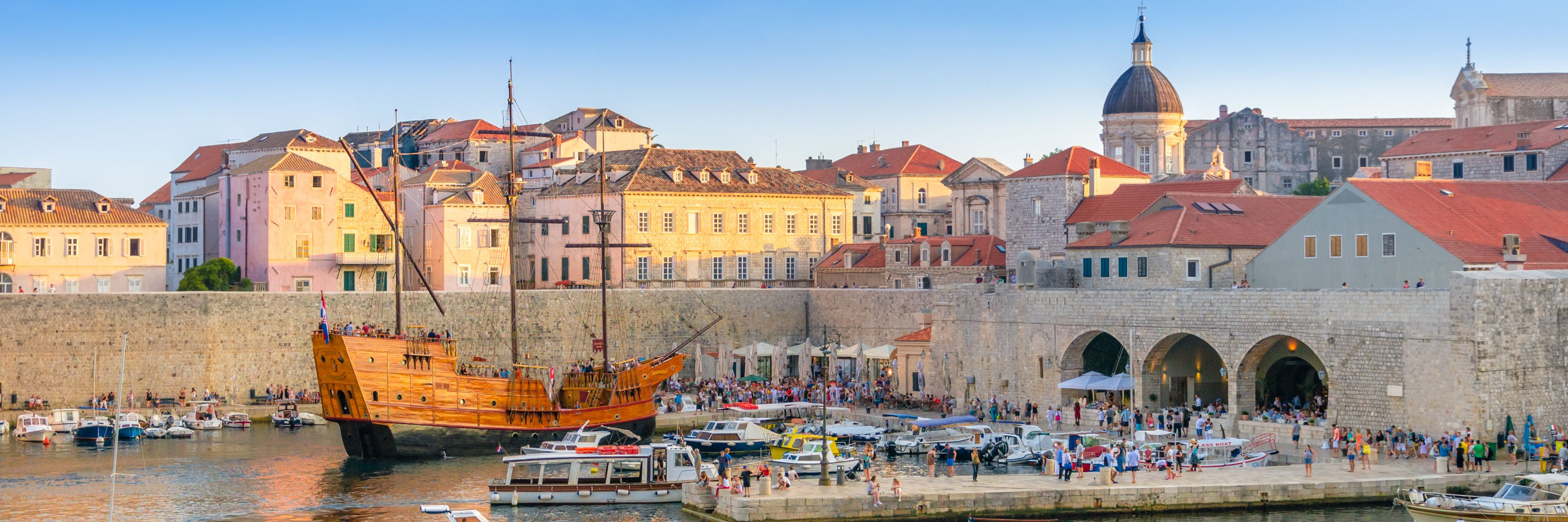 Small boats surrounding a wooden ship in a small marina at the edge of the city.