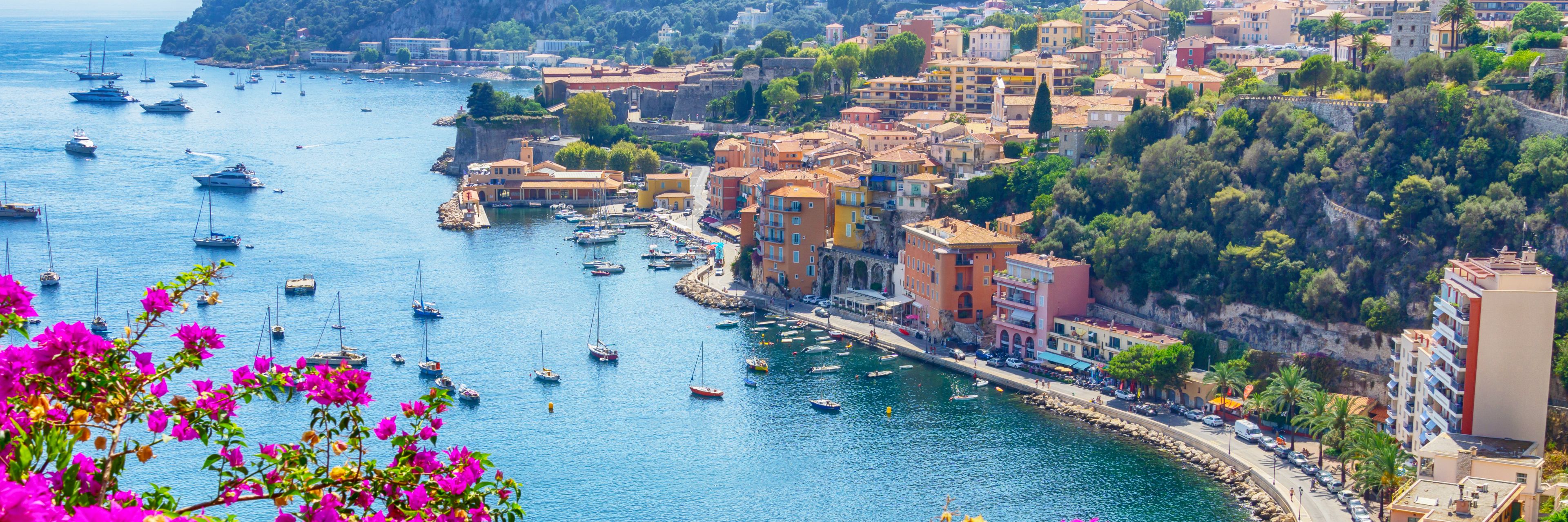 A sky view of the city facing the ocean, a variety of boats anchored.