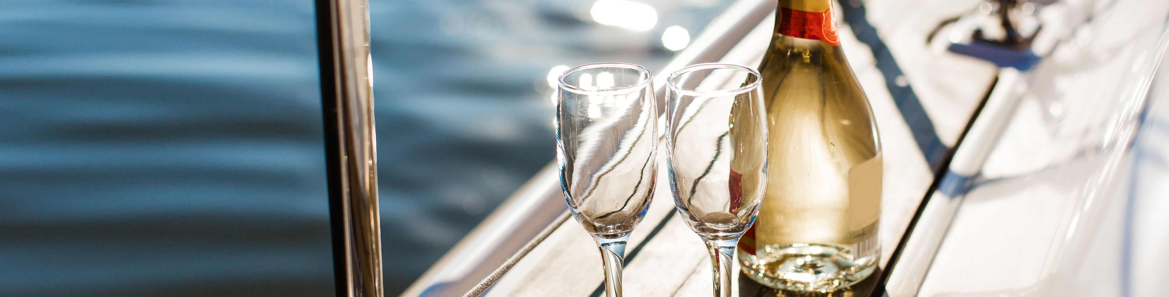Champagne glasses sit on a boat with ocean waters in the background.