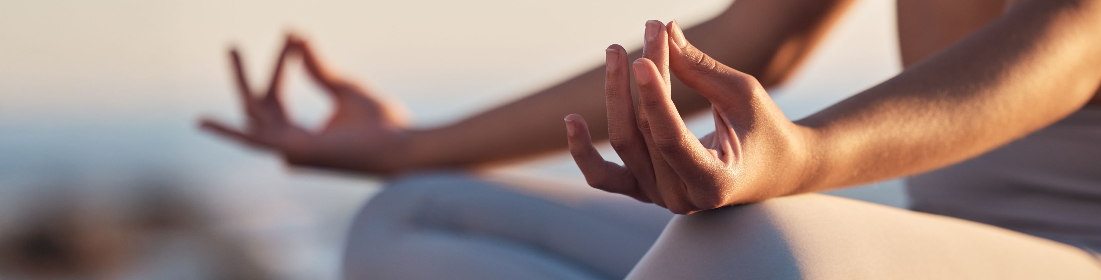 Person sitting criss cross while holding a meditating position.