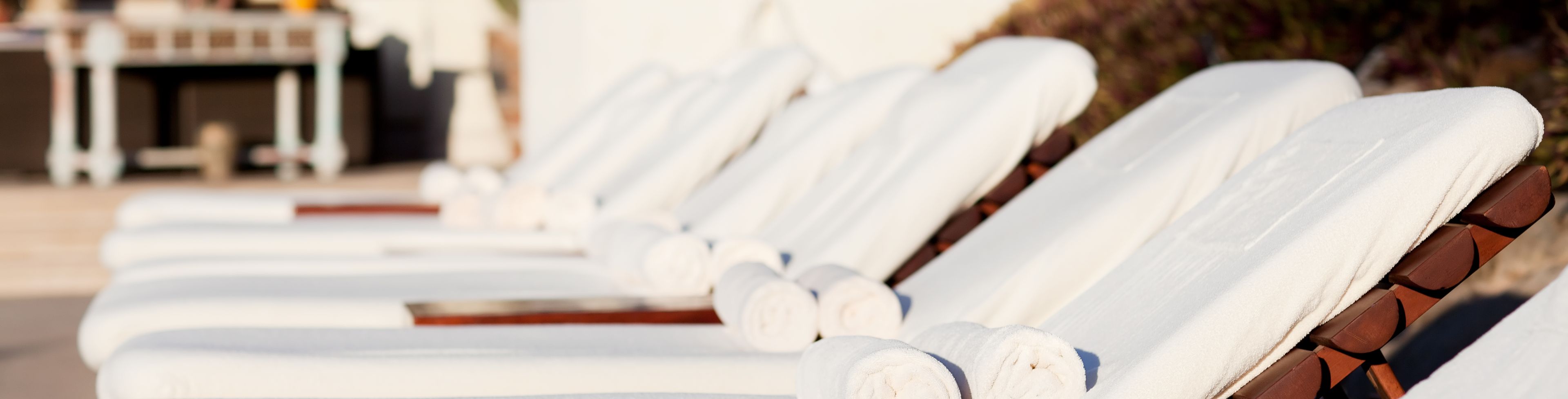 Towels sit both laid out and folded on pool lounge chairs.