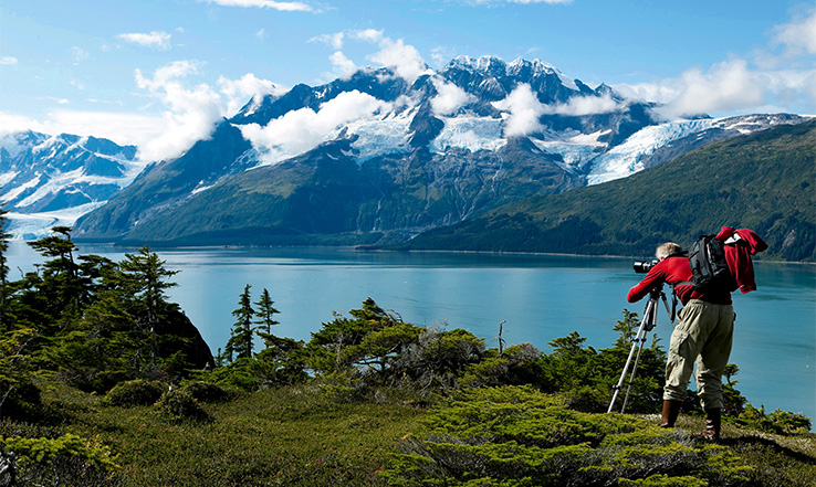 Person taking a photo from a camera, with mountains and water in the distance.