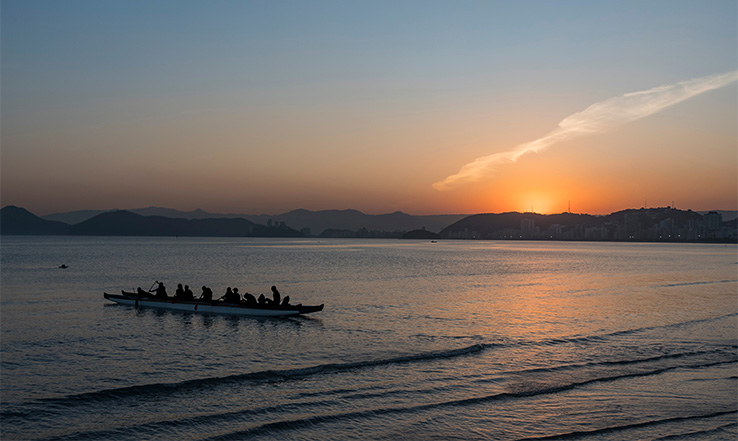 Many people in a long canoe on the ocean at sunset.