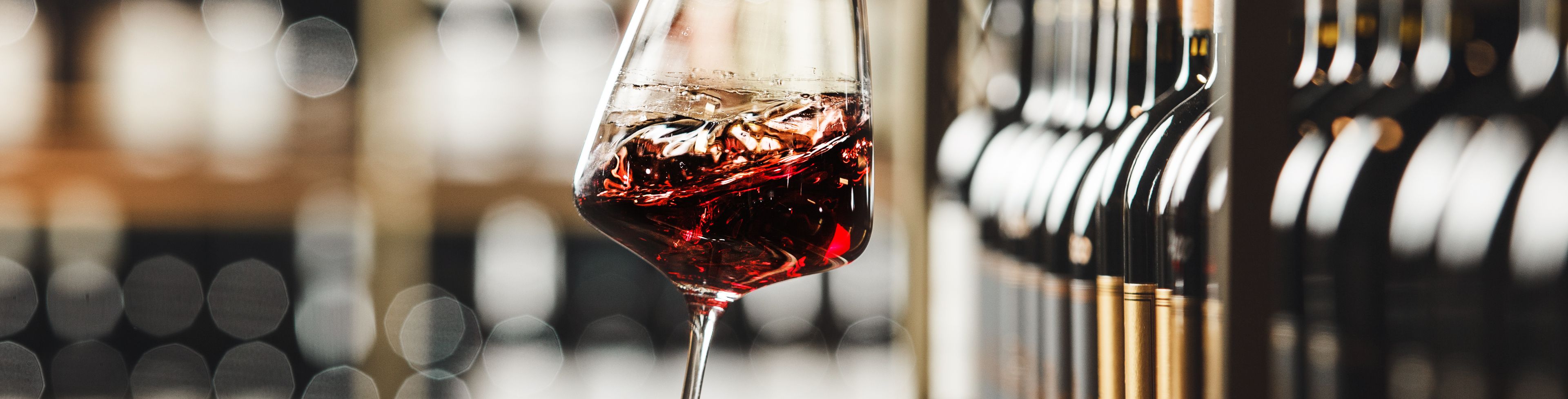 Person holding a glass of wine, near a shelf full of wine bottles.