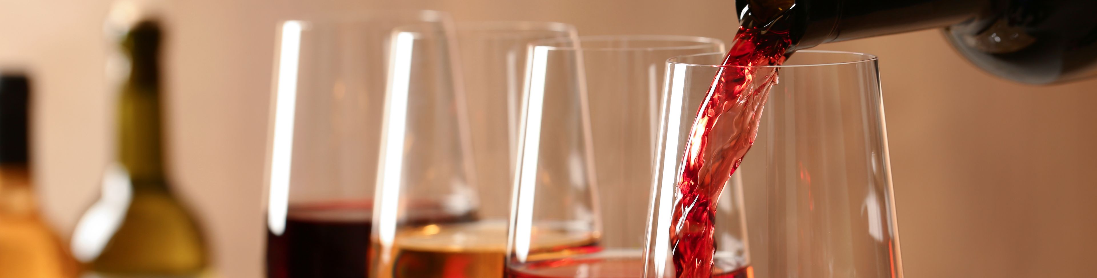 Wine being poured into a wine glasses that are lined up.