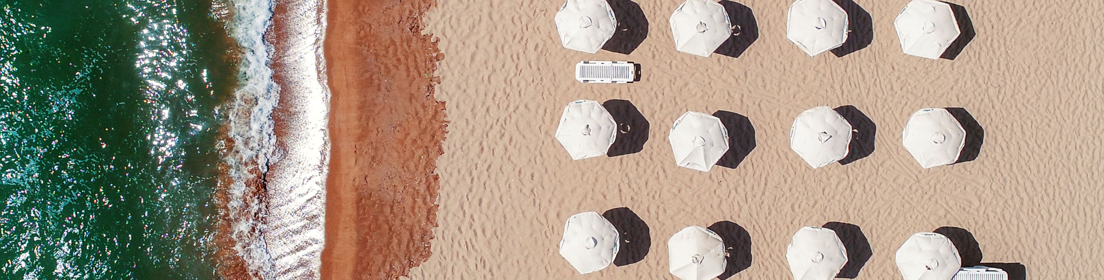 Beach umbrellas sit arranged in front of deep blue ocean waters.