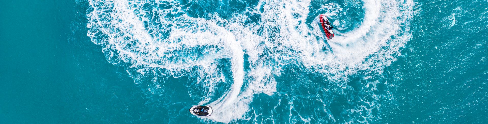 Two people on two jet skis driving on the water around each other. 
