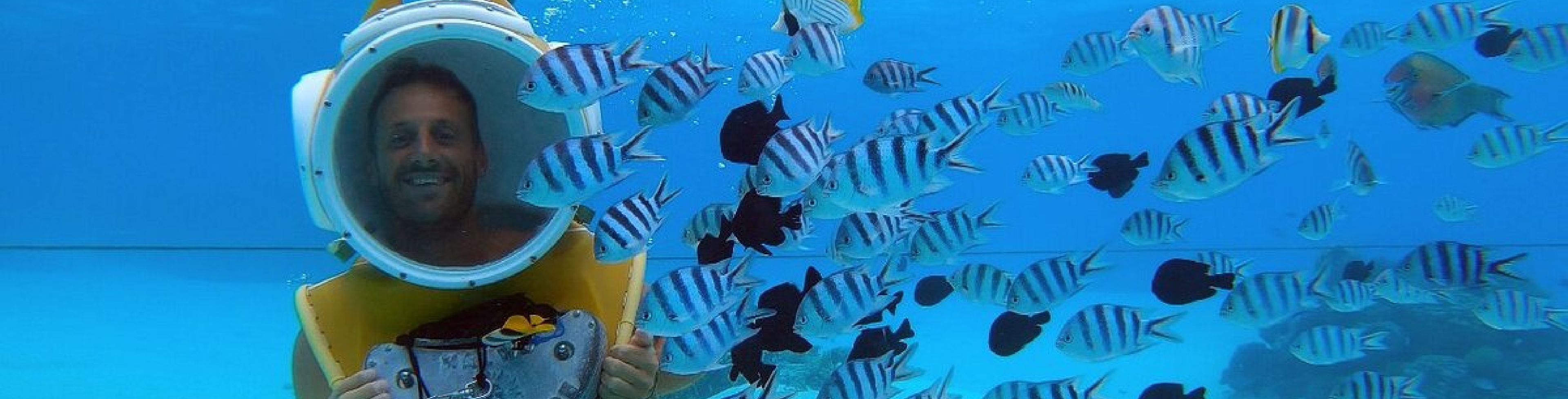Woman with a scuba helmet on, walking underwater.