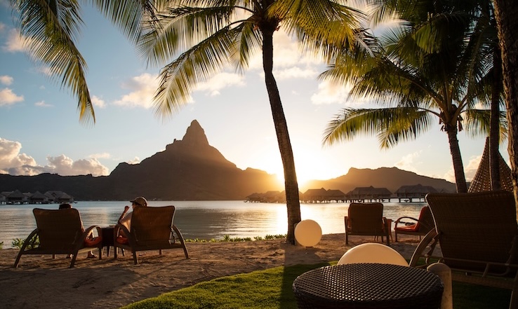 People in lounge chairs at sunset on a beach.