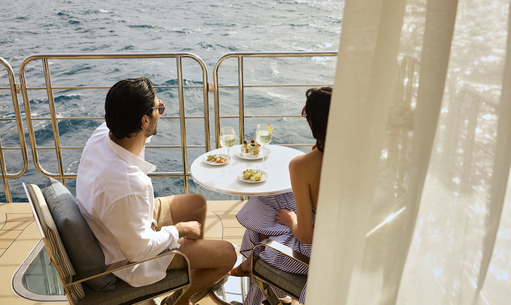 People enjoying food at a table on a deck, overlooking the sea.