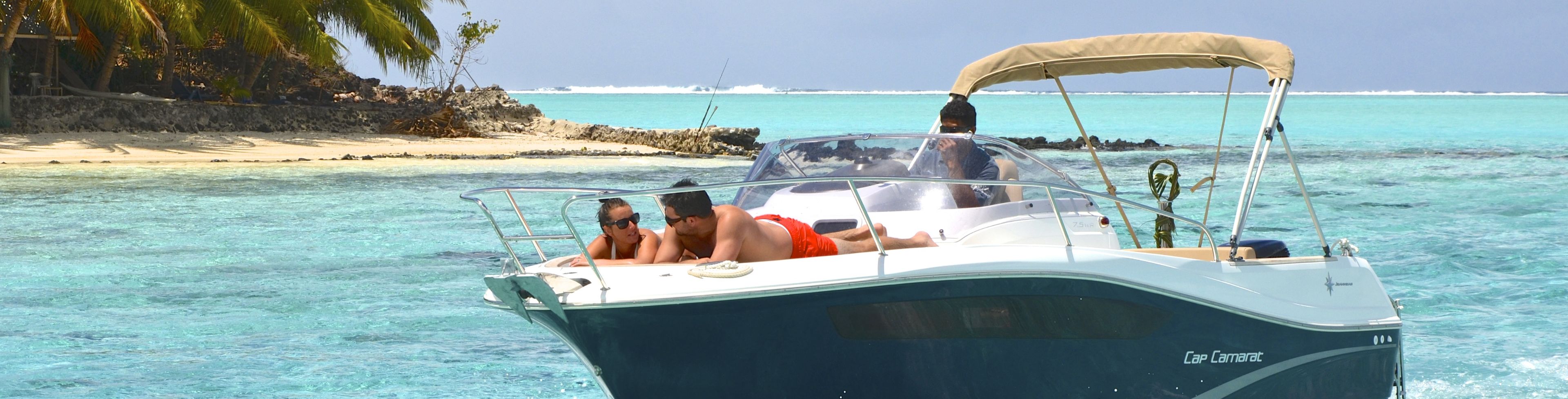 Man and woman lounging on the front of a speed boat while someone else drives the boat.