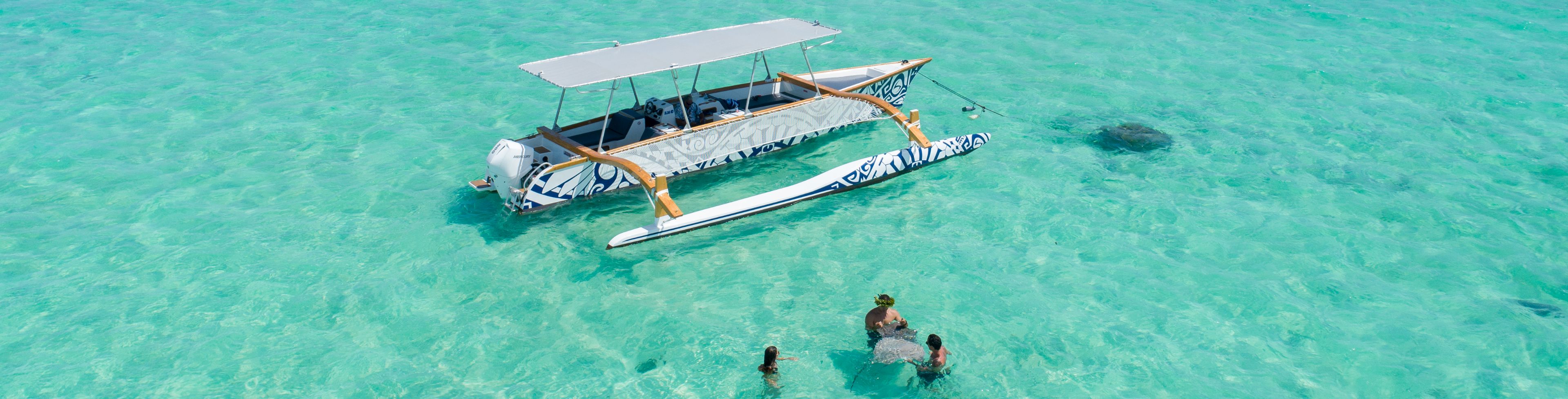 Anchored boat with people swimming with a manta ray next to it.