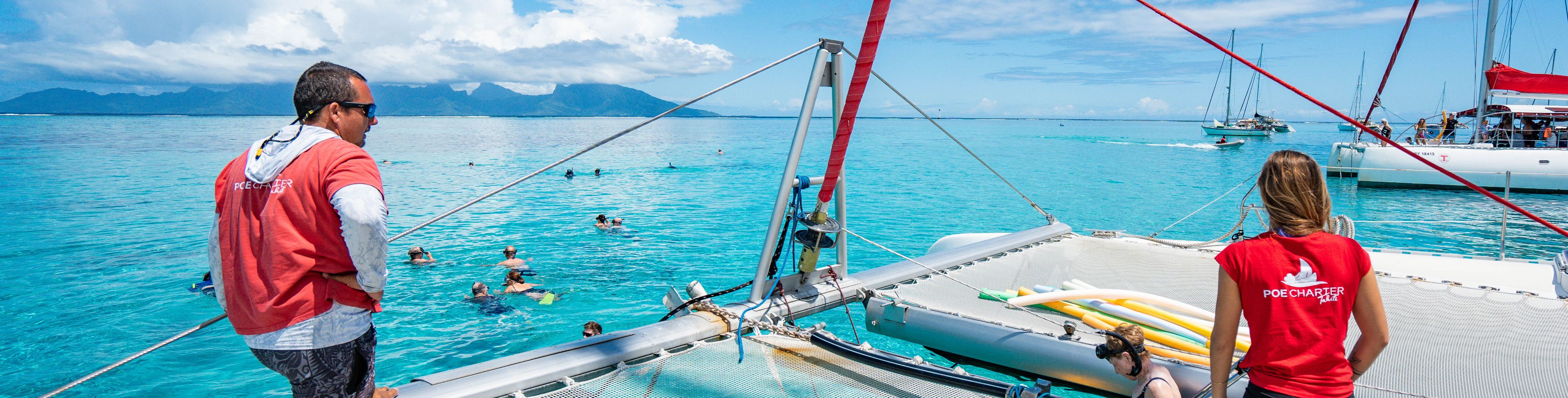 People on and swimming around anchored sail boats.